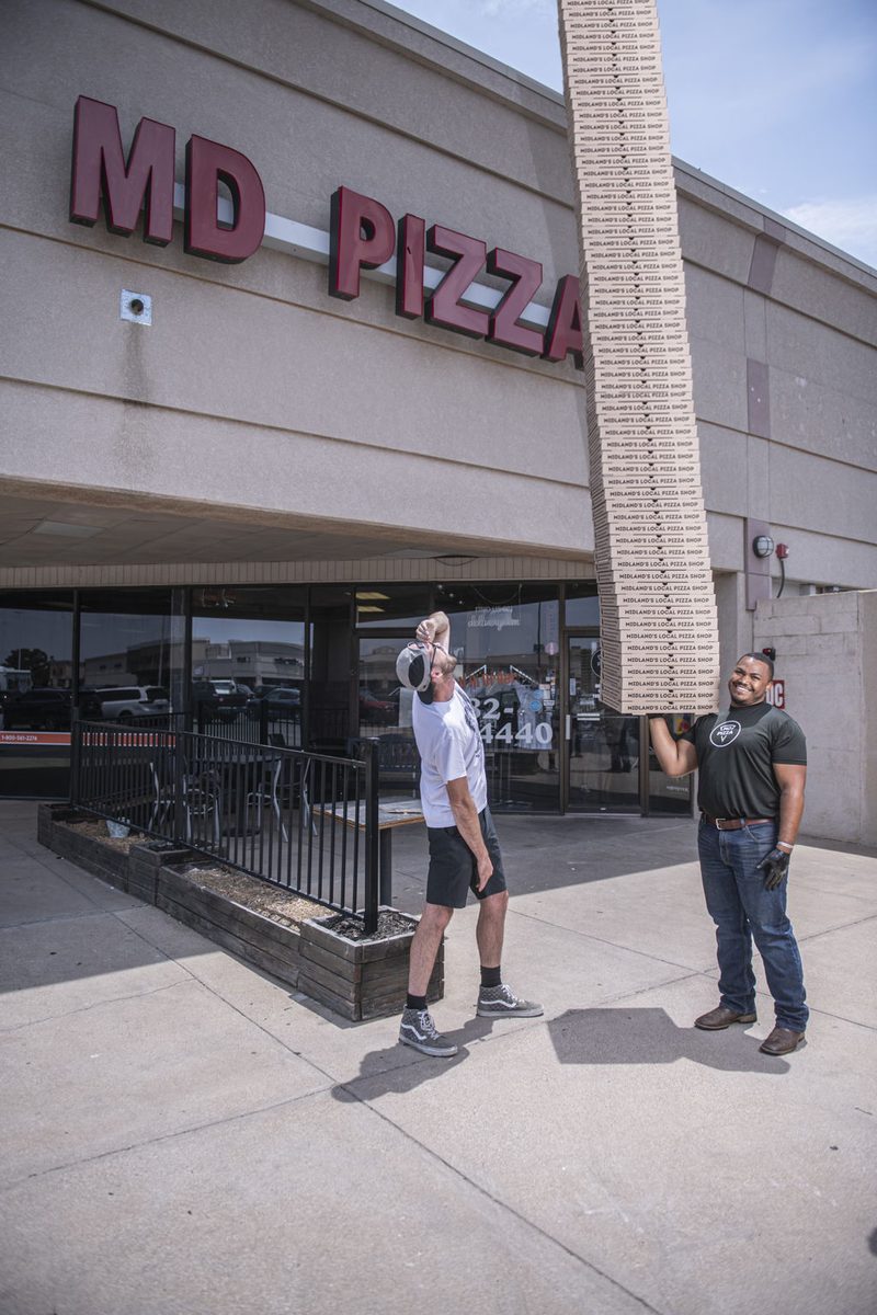 Midland Pizza Factory owners outside the shop holding a towering stack of pizza boxes